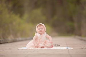 Cheeky baby girl in peach bonnet sitting on boardwalk