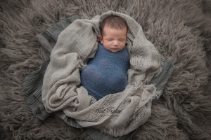 cheeky baby boy wrapped in blue blanket on gray fur