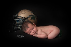 Cheeky baby boy laying next to Michigan state football helmet signed by Mark Dantonio