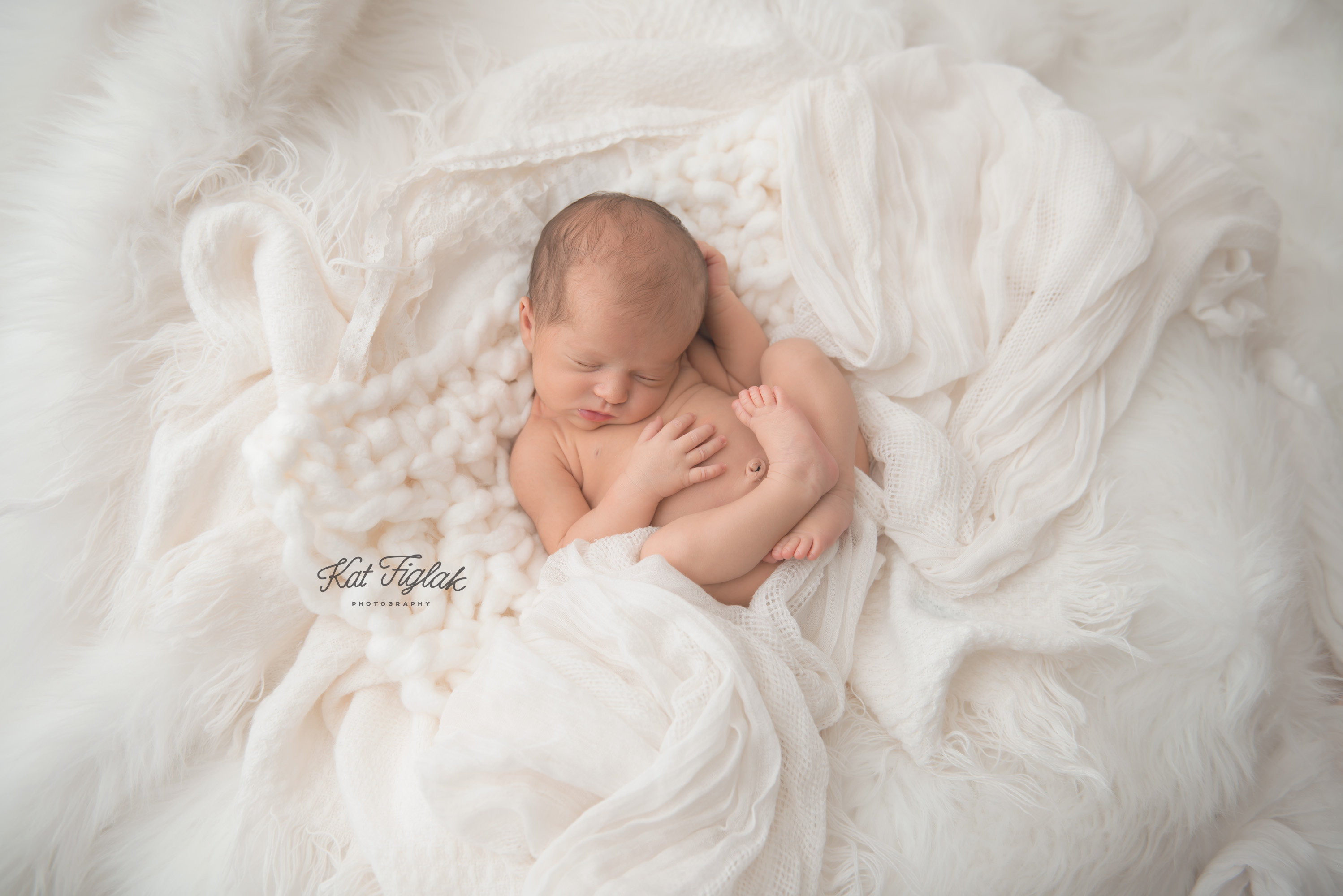 newborn baby girl sitting in layers of soft blankets and knits sleeping
