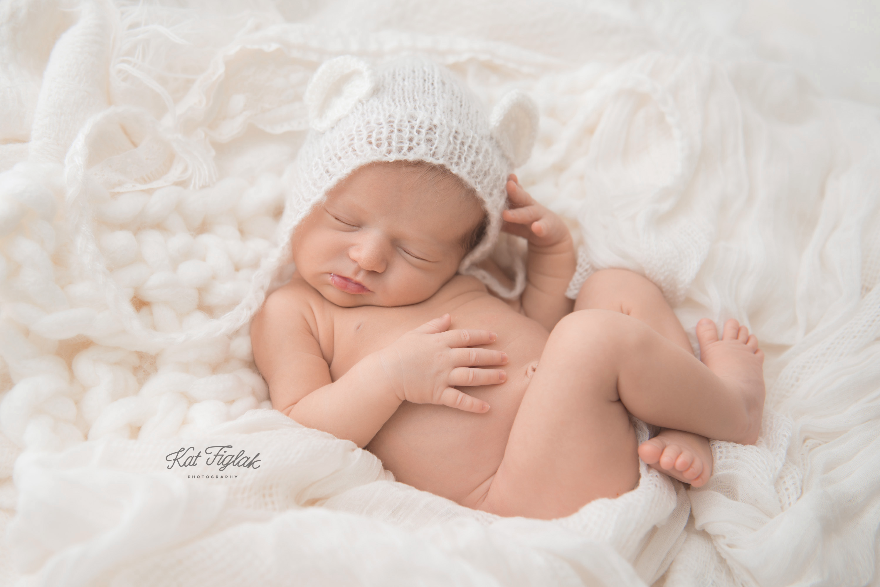 newborn baby girl sleeping in soft white blankets and knits with a bear hat on