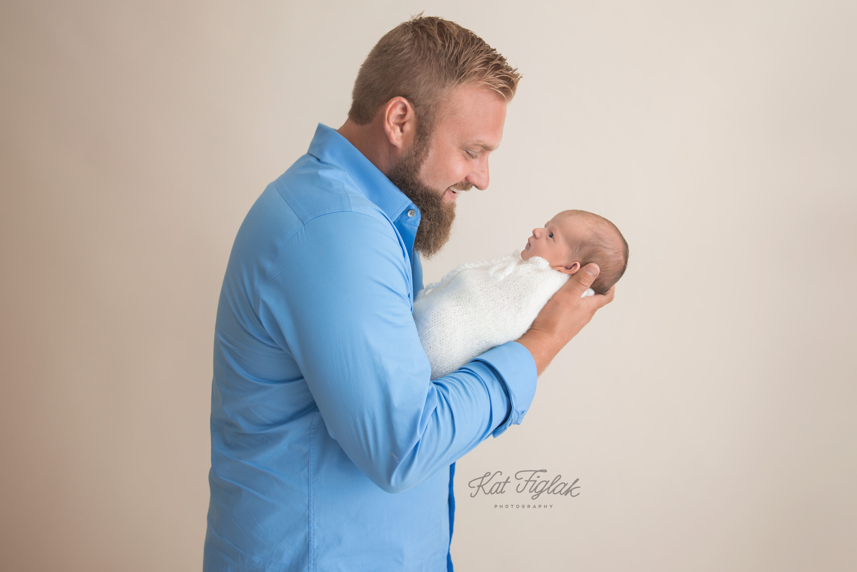 new dad holding his newborn baby girl wearing a blue shirt with a tan background