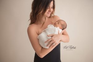 new mom holding her newborn baby girl wearing a black dress standing by a