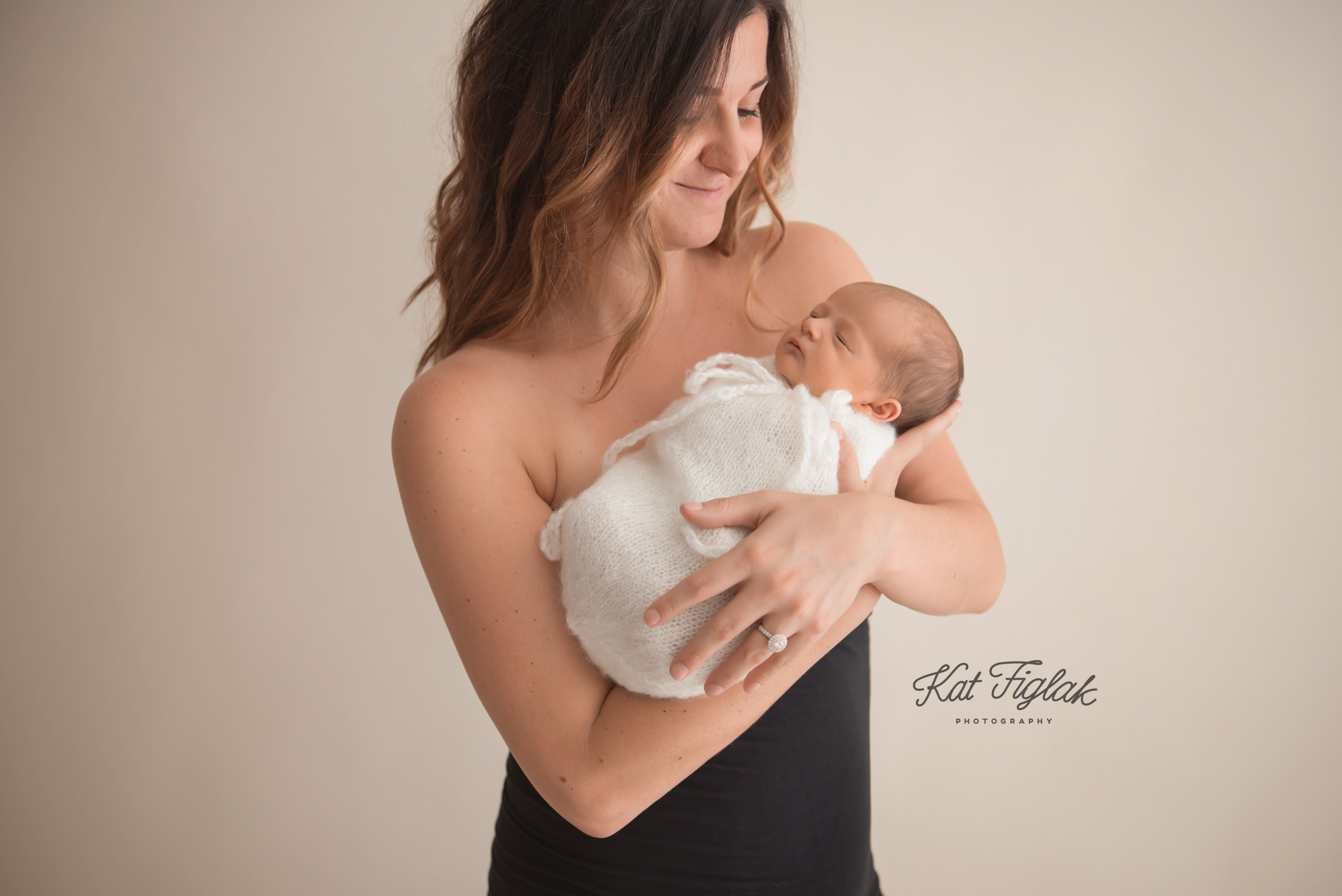new mom holding her newborn baby girl wearing a black dress standing by a 
