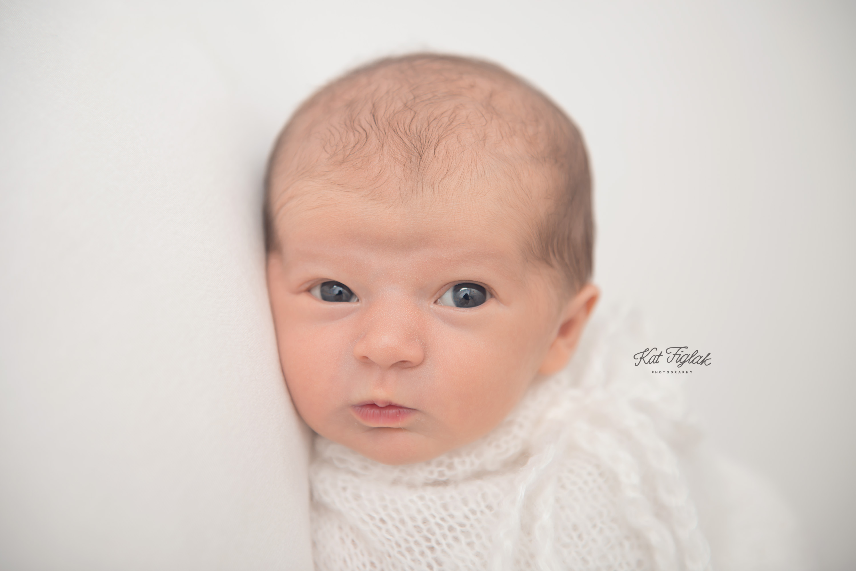 baby girl awake and bright eyed wrapped in white knit laying on white organic blanket