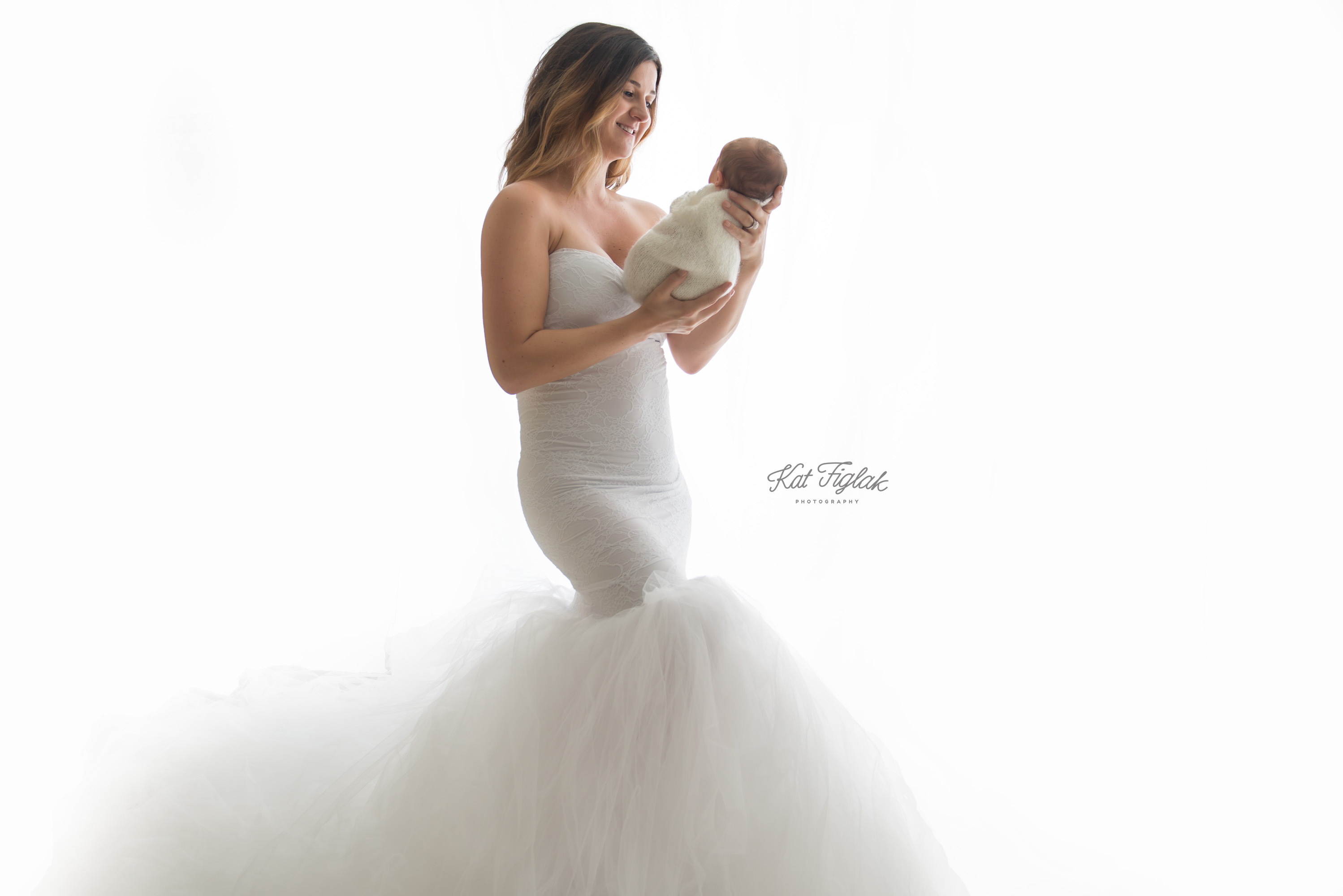 new mom holding her newborn baby while wearing a white gown with a white background