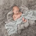 Newborn baby boy snuggled sleeping in gray blankets, knits and furs wrapped in light blue wrap