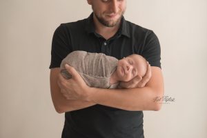 Newborn baby boy wrapped in tan knit smiling in dads arms