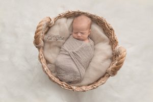 newborn baby boy wrapped in tan wrap laying in a basket on a cream fur