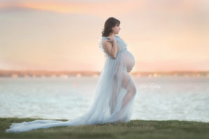 Pregnant mom with twins in front of lake sunset wearing blue dress