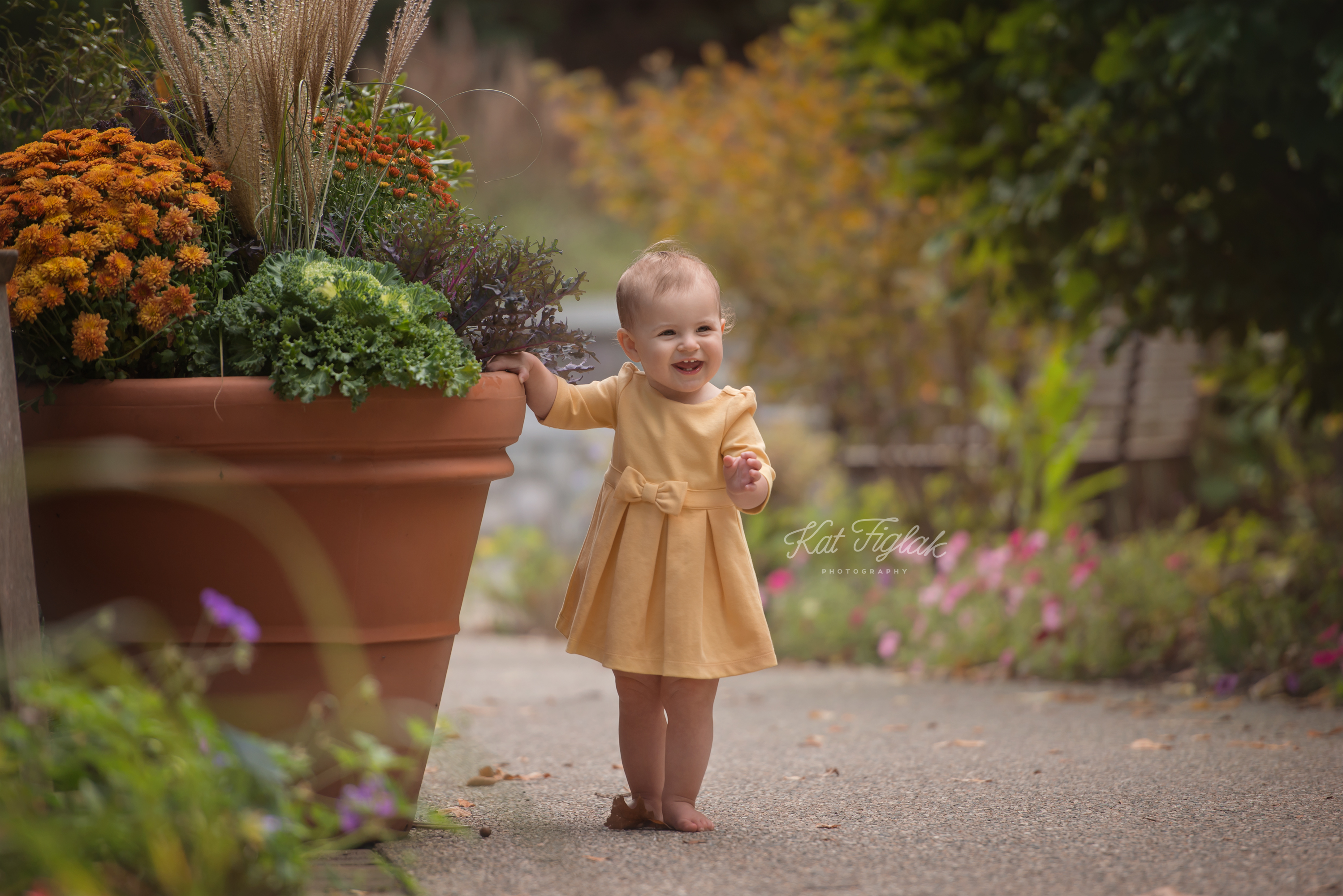 one year old baby girl smiling holding flower pot wearing a yellow dress