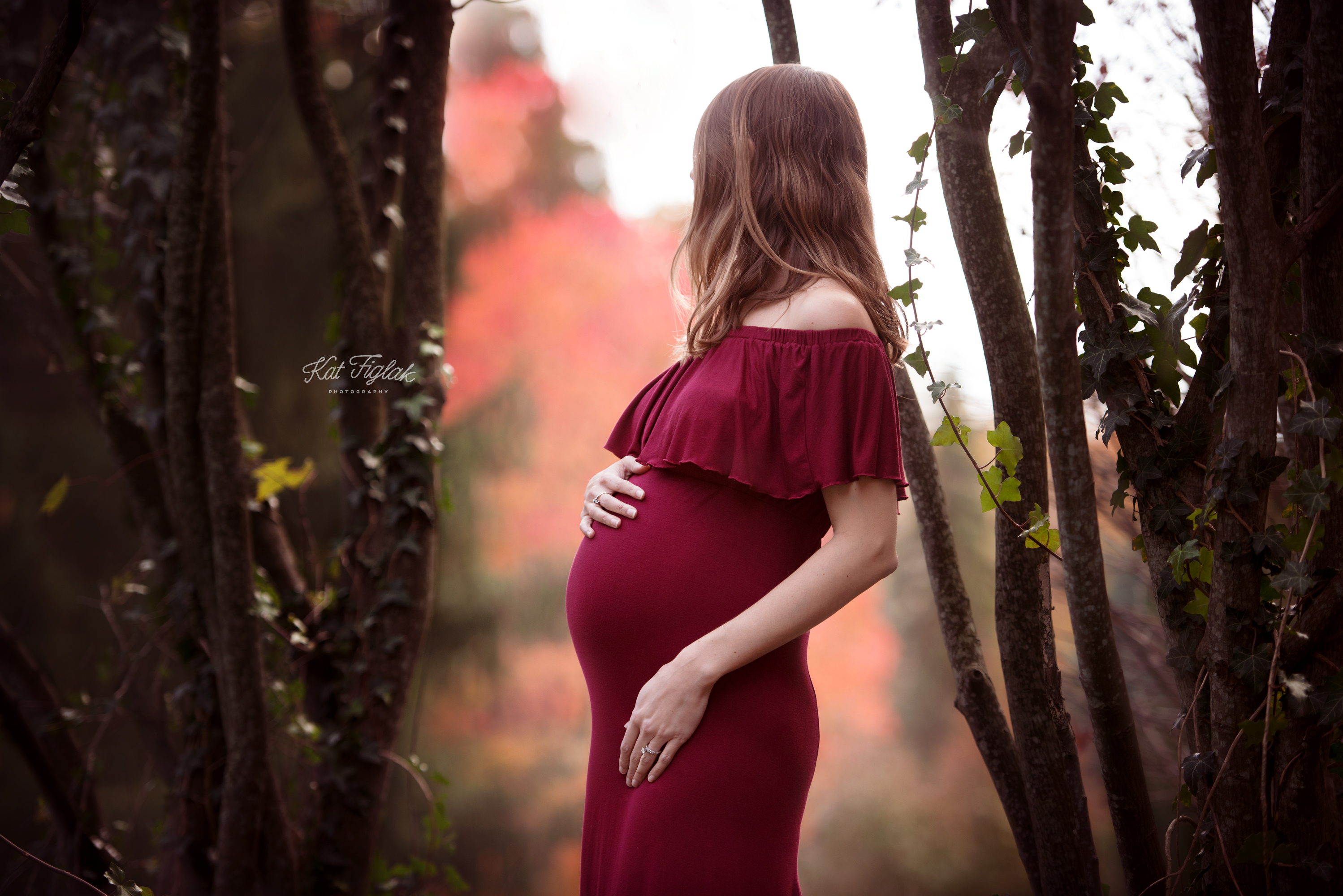 pregnant mom standing with cranberry dress on with fall colors in the background