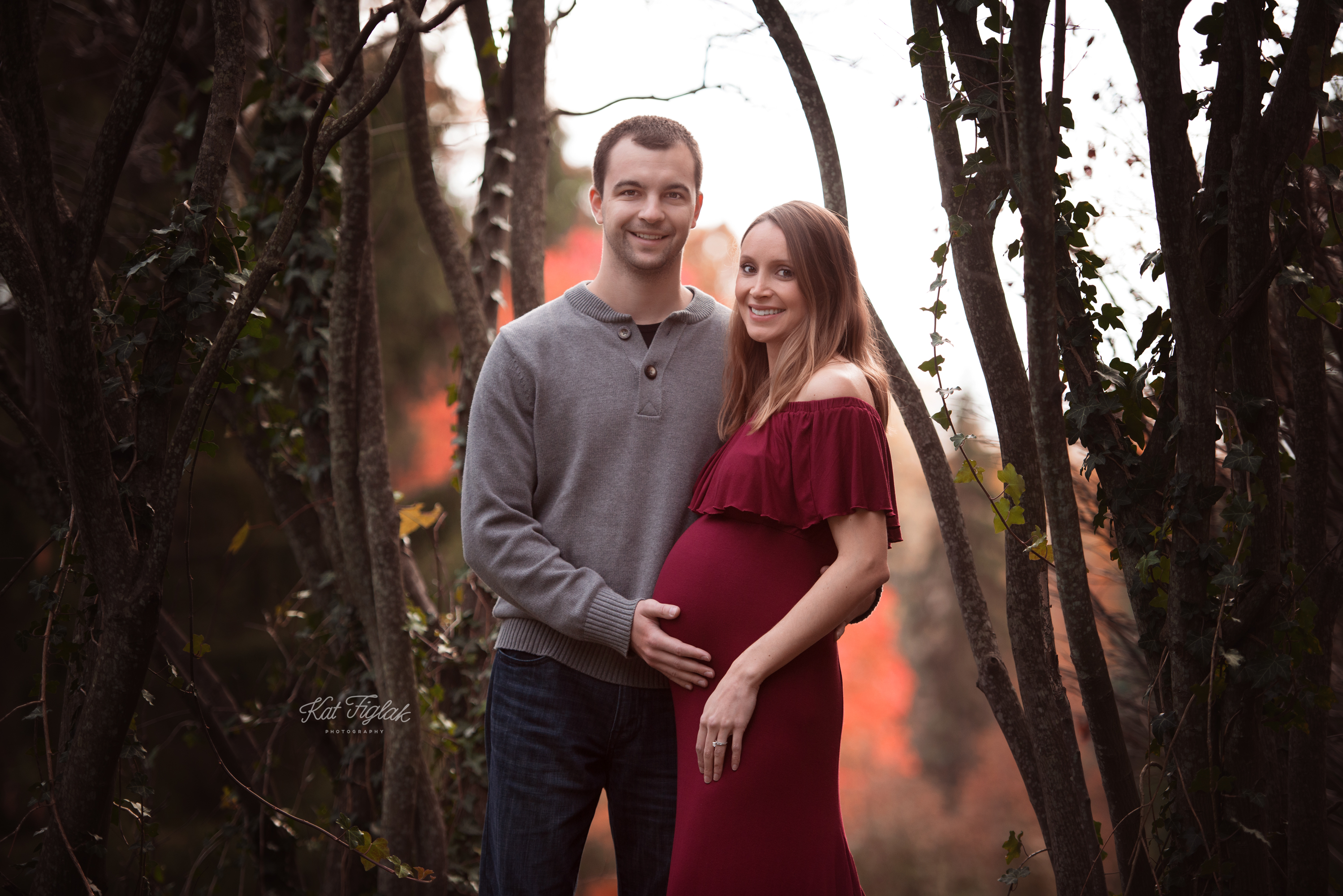expecting couple smiling together with fall colors in the background