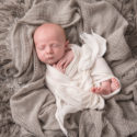 baby wrapped in cream wrap laying in gray blankets
