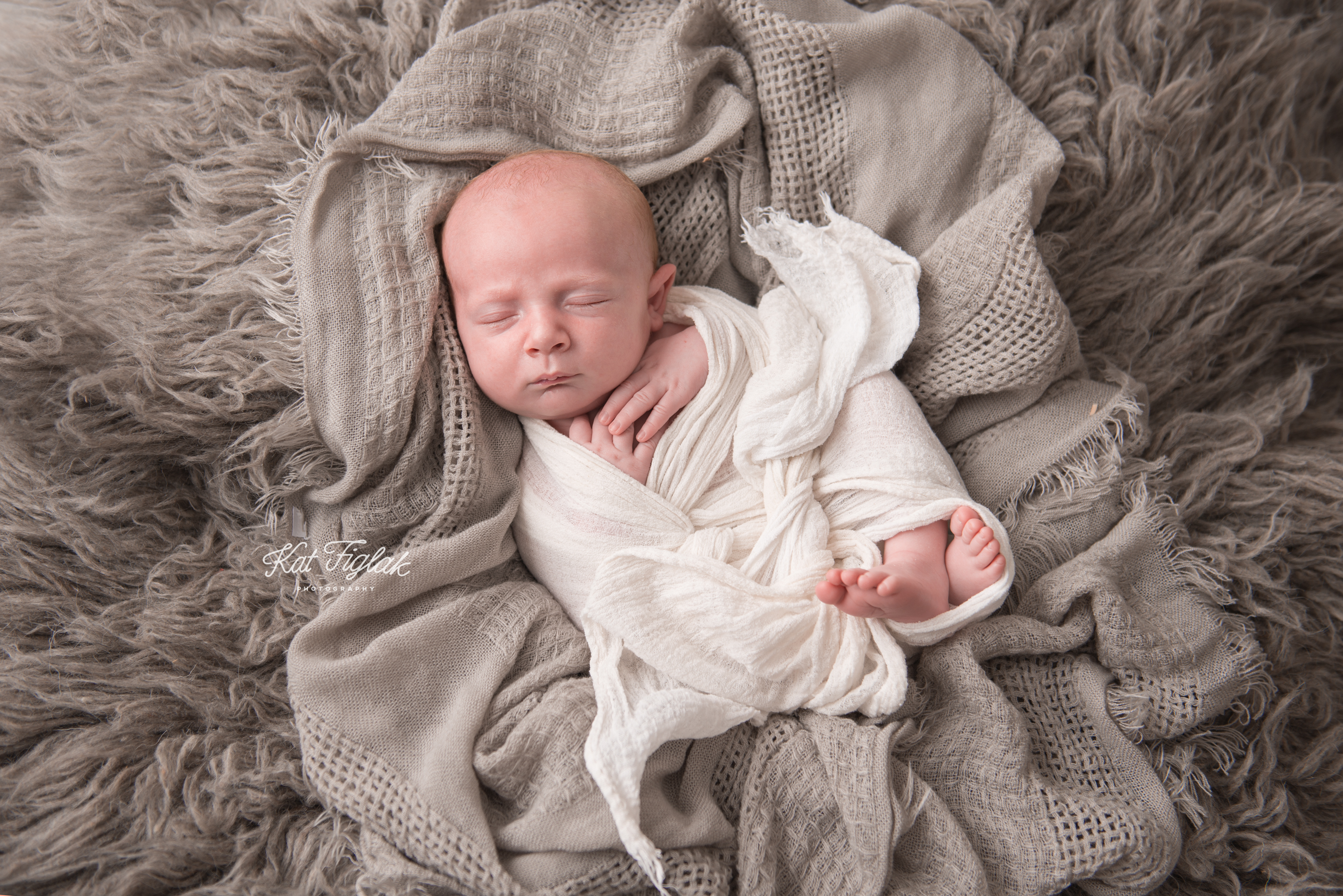 baby wrapped in cream wrap laying in gray blankets