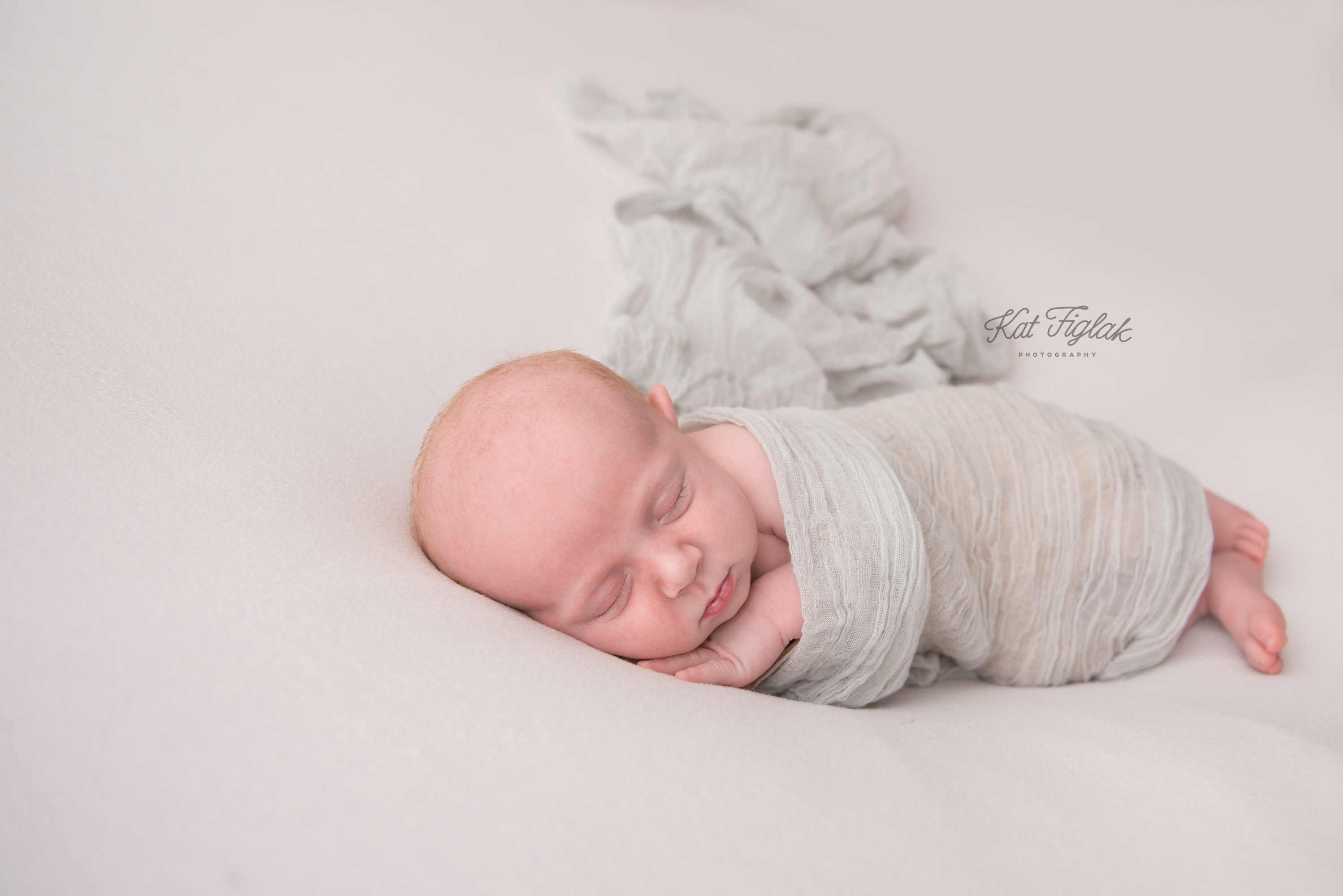 newborn baby boy sleeping on white blanket covered in gray wrap