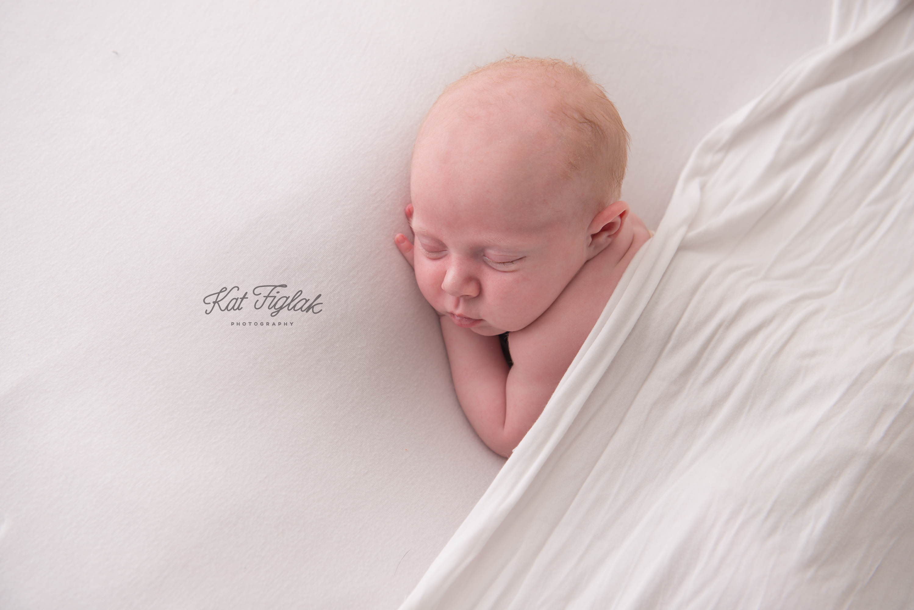 newborn baby boy laying on white blanket covered by white wrap sleeping