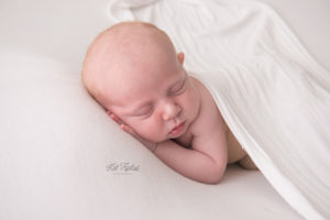 Newborn baby boy laying on white drop covered by white wrap