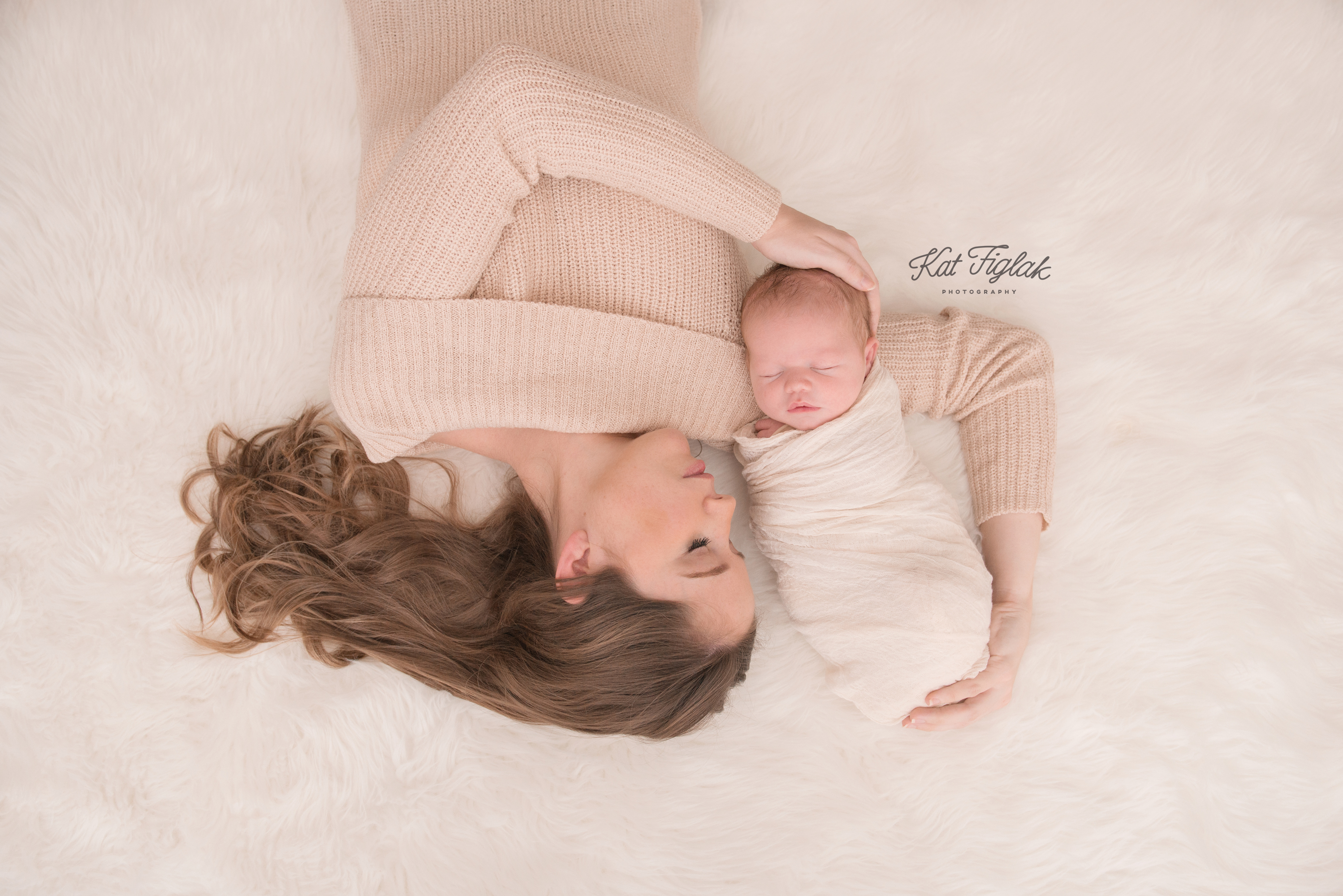 mom holding her newborn son laying on fur rug baby wrapped in cream wrap