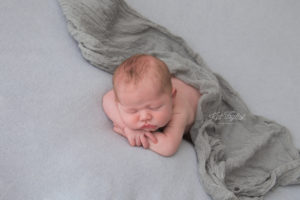 baby boy laying on light blue fabric draped with gray wrap