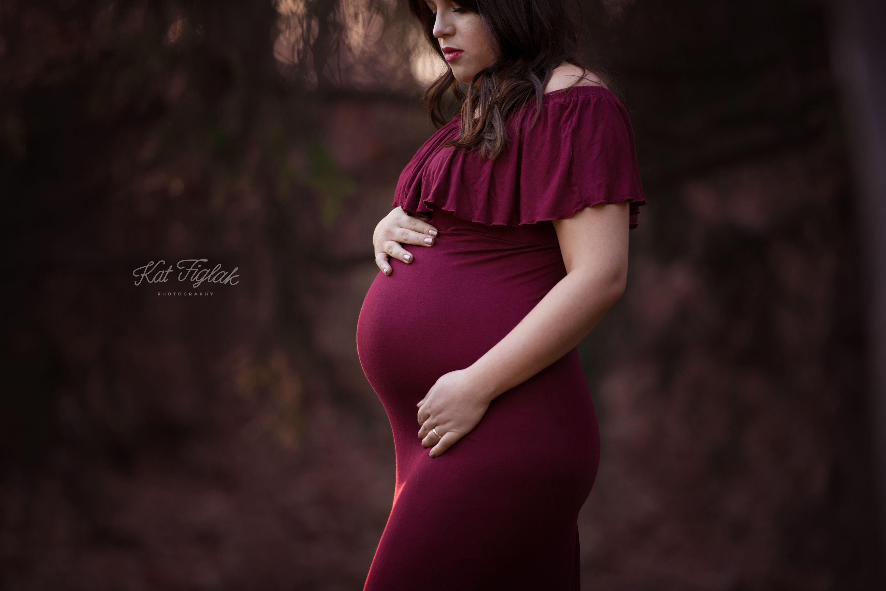 Mother to be dressed in cranberry colored dress standing