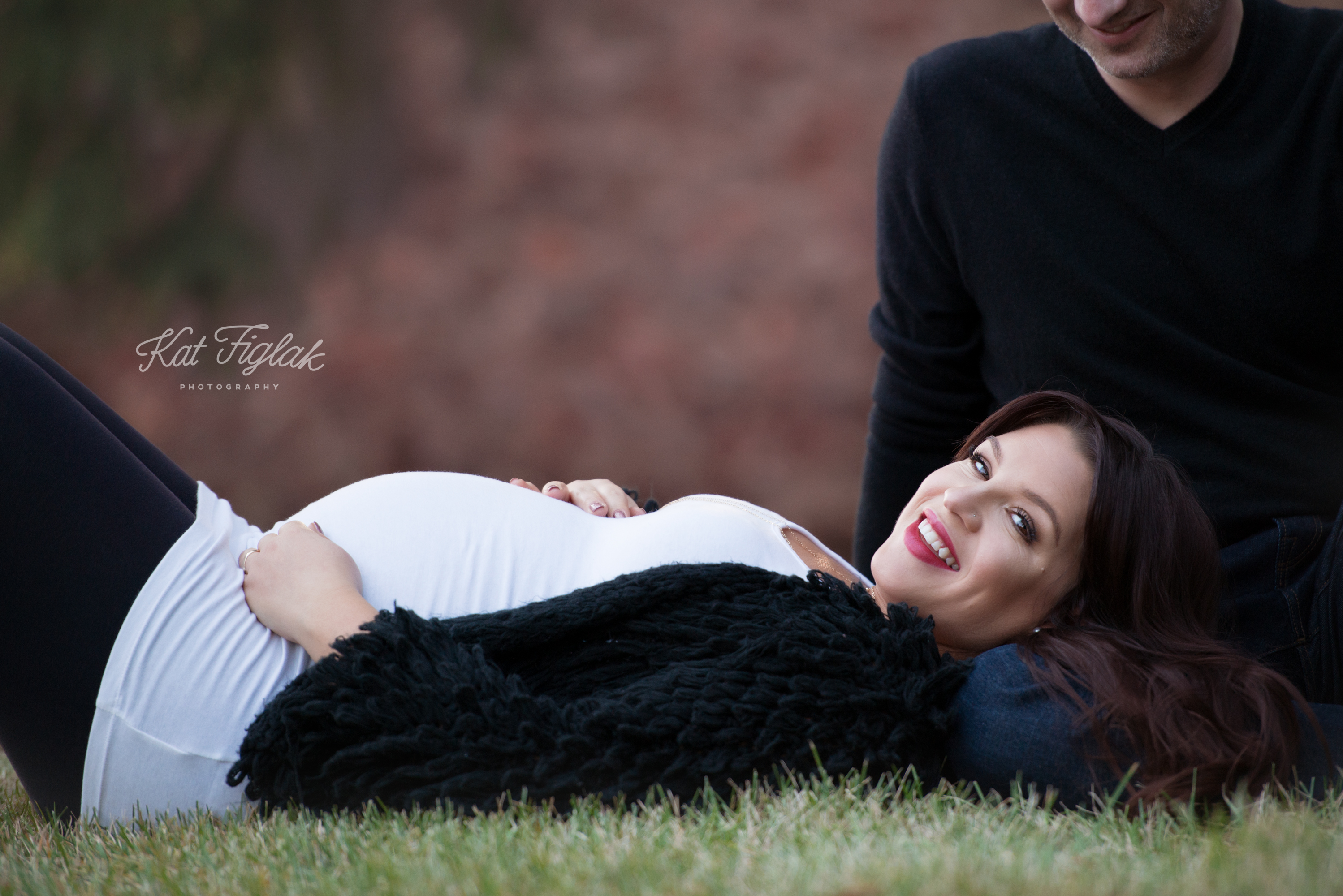 pregnant mom wearing a white tank top and black sweater laying down with head on husbands lap