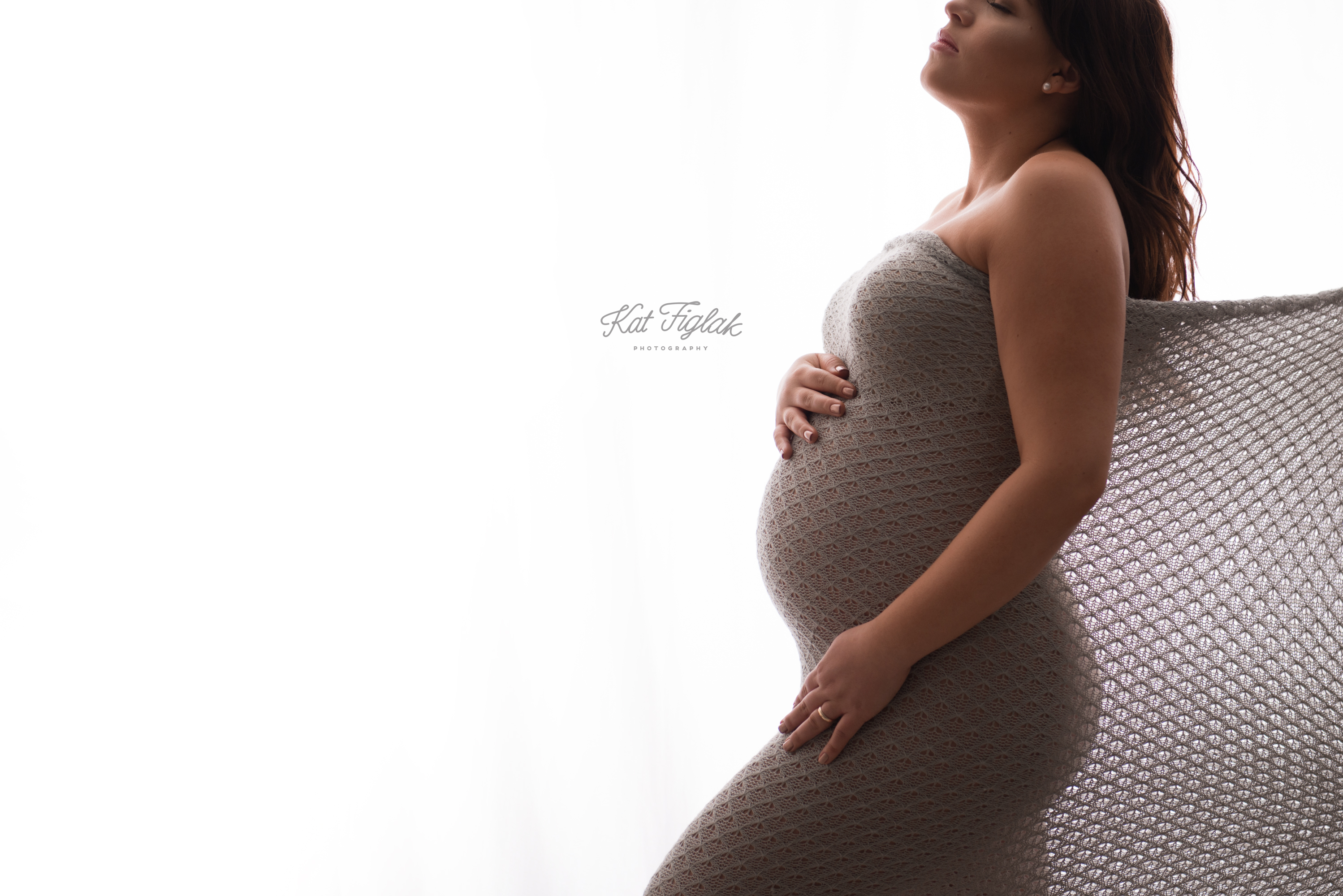 backlit silhouette photo of a pregnant woman draped in gray knit fabric wrap