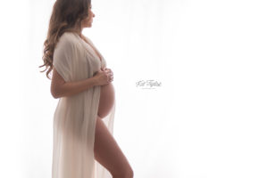 backlit maternity photo mom to be with bare belly draped with sheer cream fabric