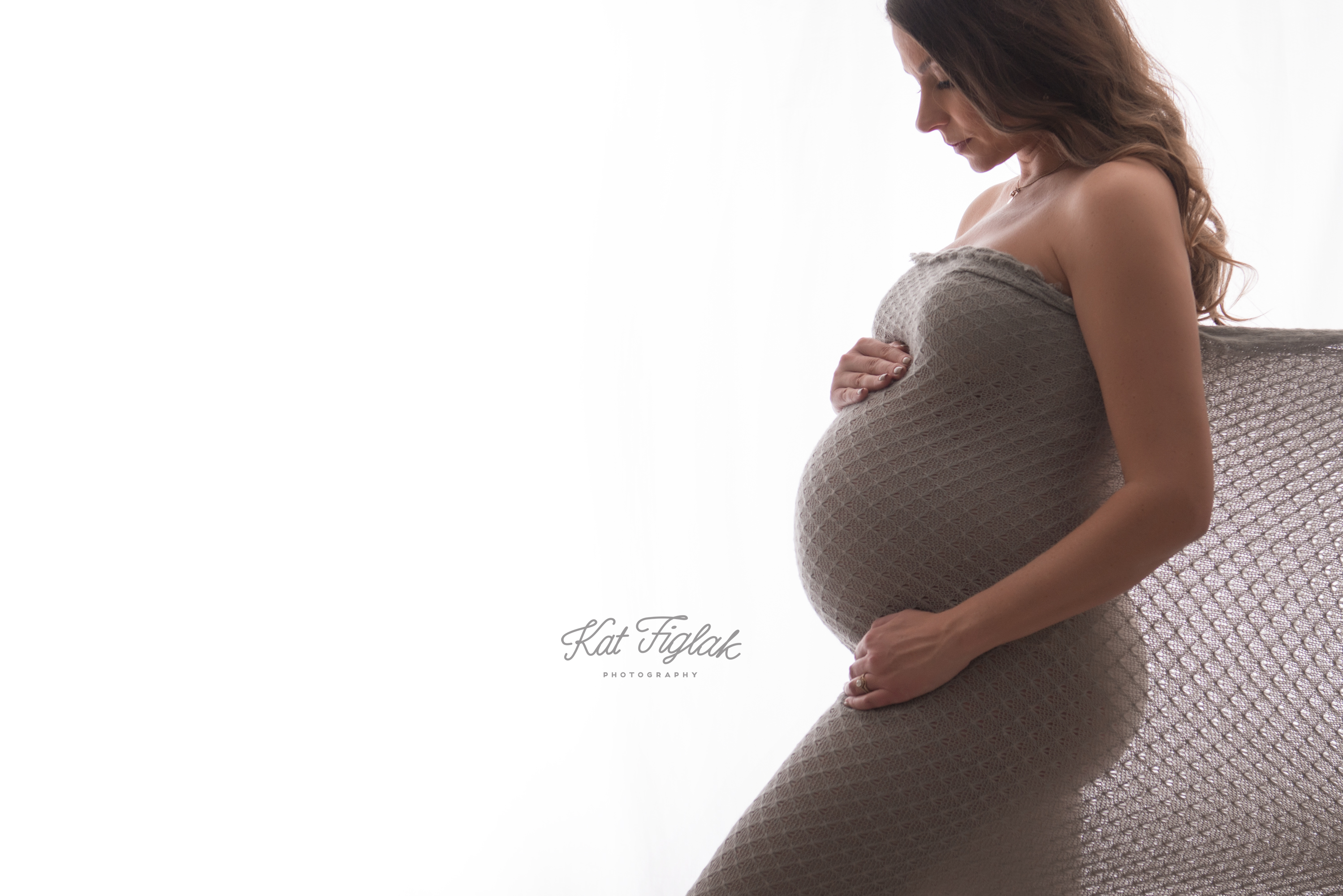 maternity silhouette shot mom draped in gray fabric looking down at her belly