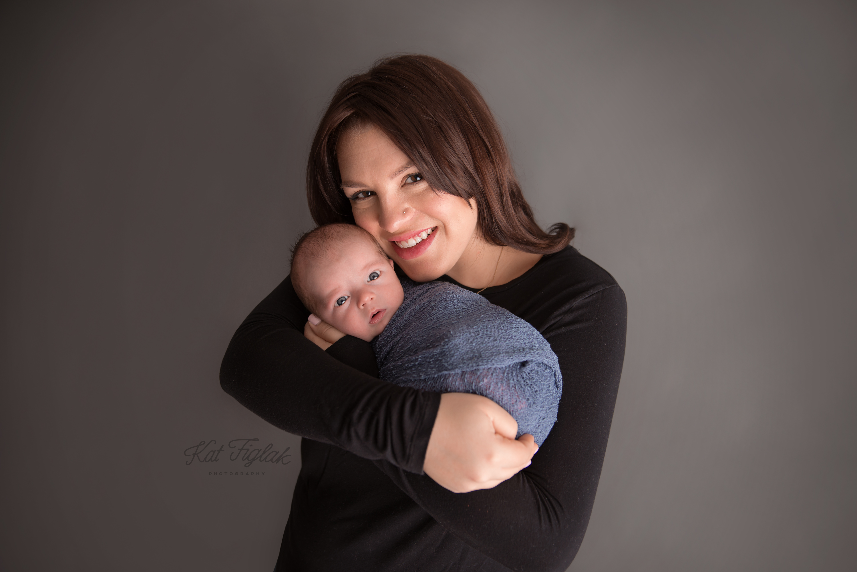 smiling mom holding her newborn son baby wrapped in blue wrap