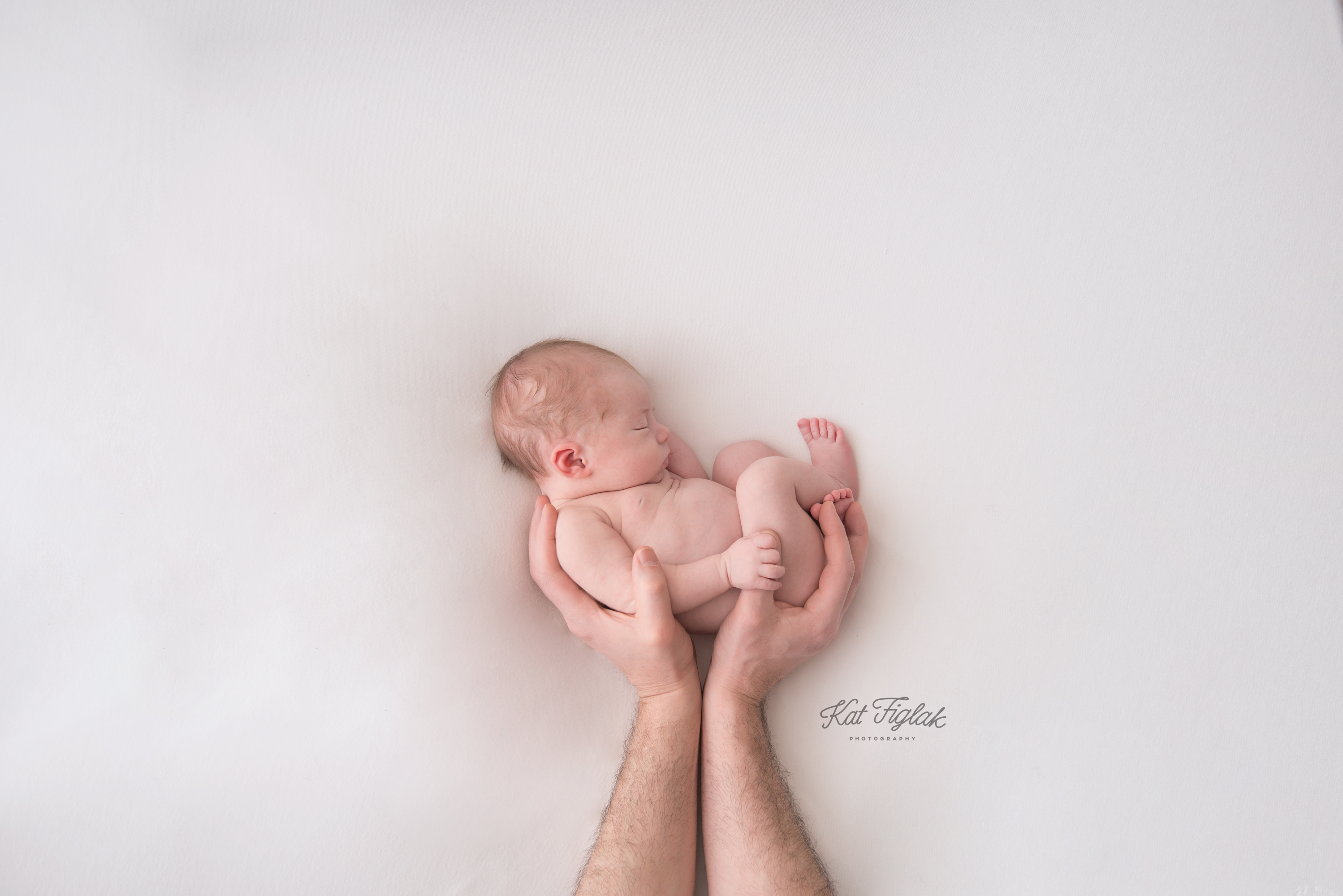 newborn baby boy sleeping in dads hands on a white backdrop