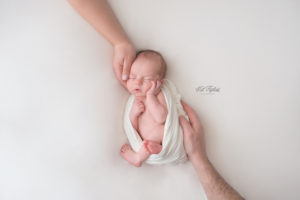 newborn baby boy sleeping on white blanket with both parents hands resting on him