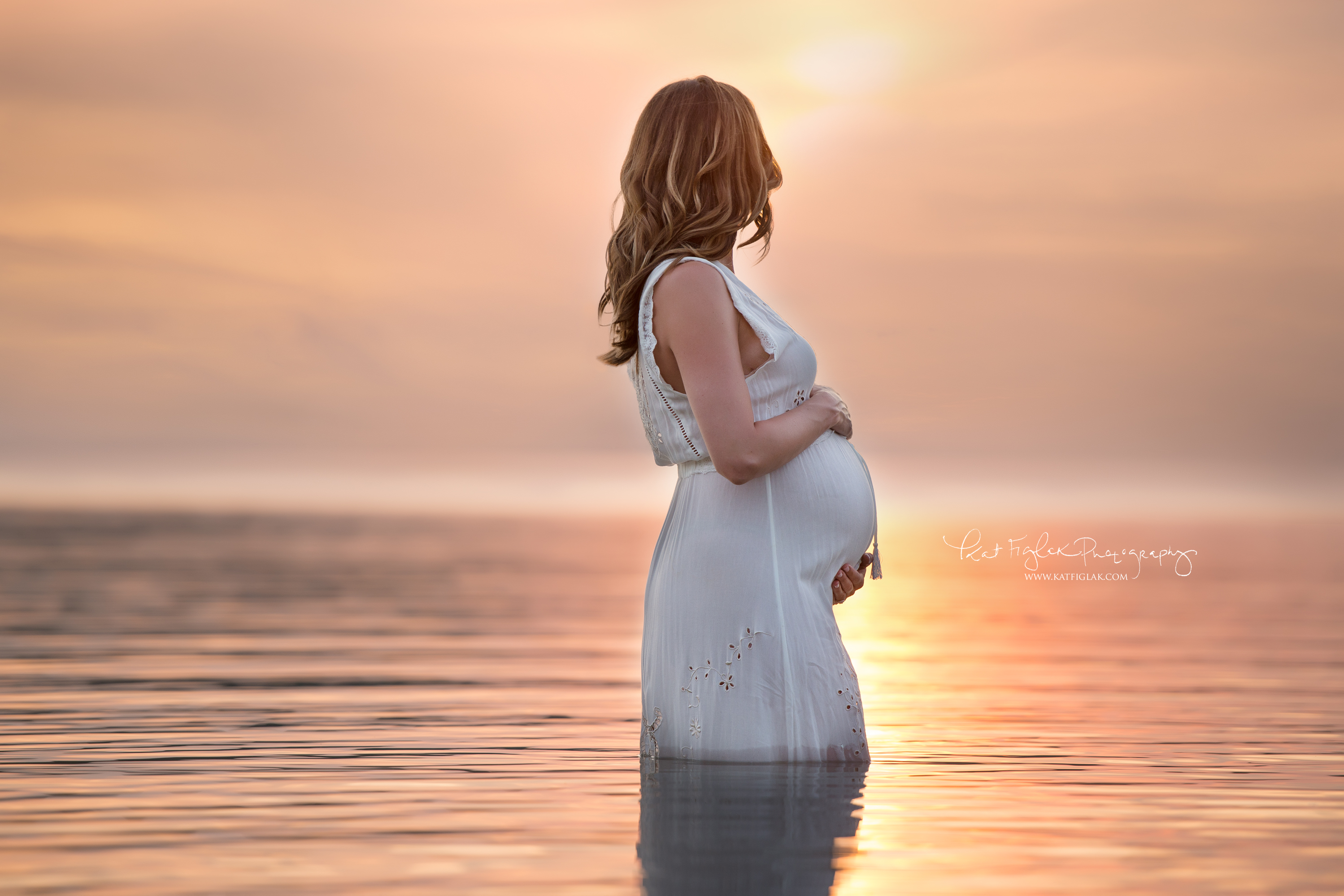 pregnant mom standing in lake with beautiful sunset
