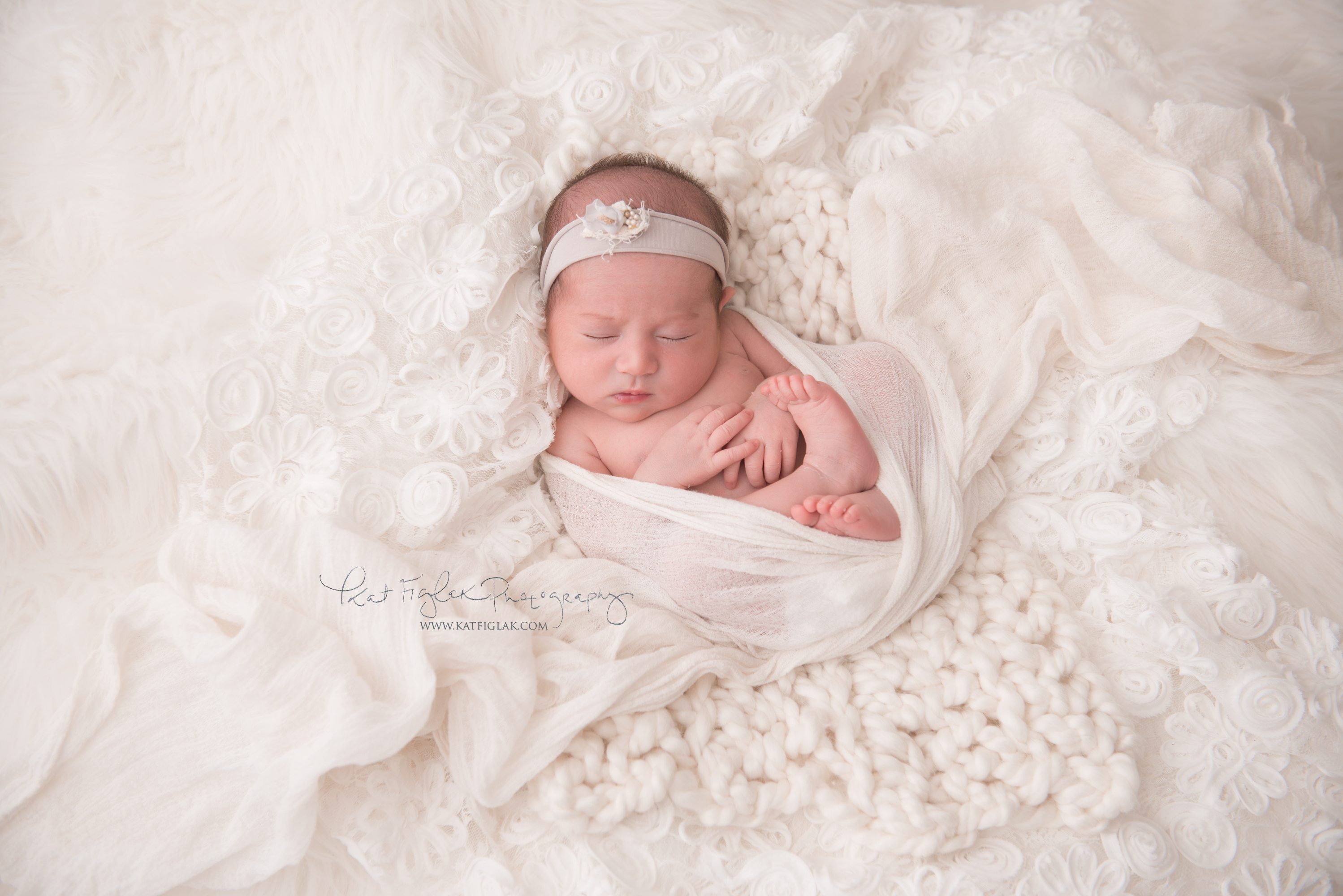 Newborn baby girl on white rug and knits sleeping with floral tieback headband