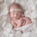 smiling newborn baby girl laying in white lace and fur wrapped in white wrap