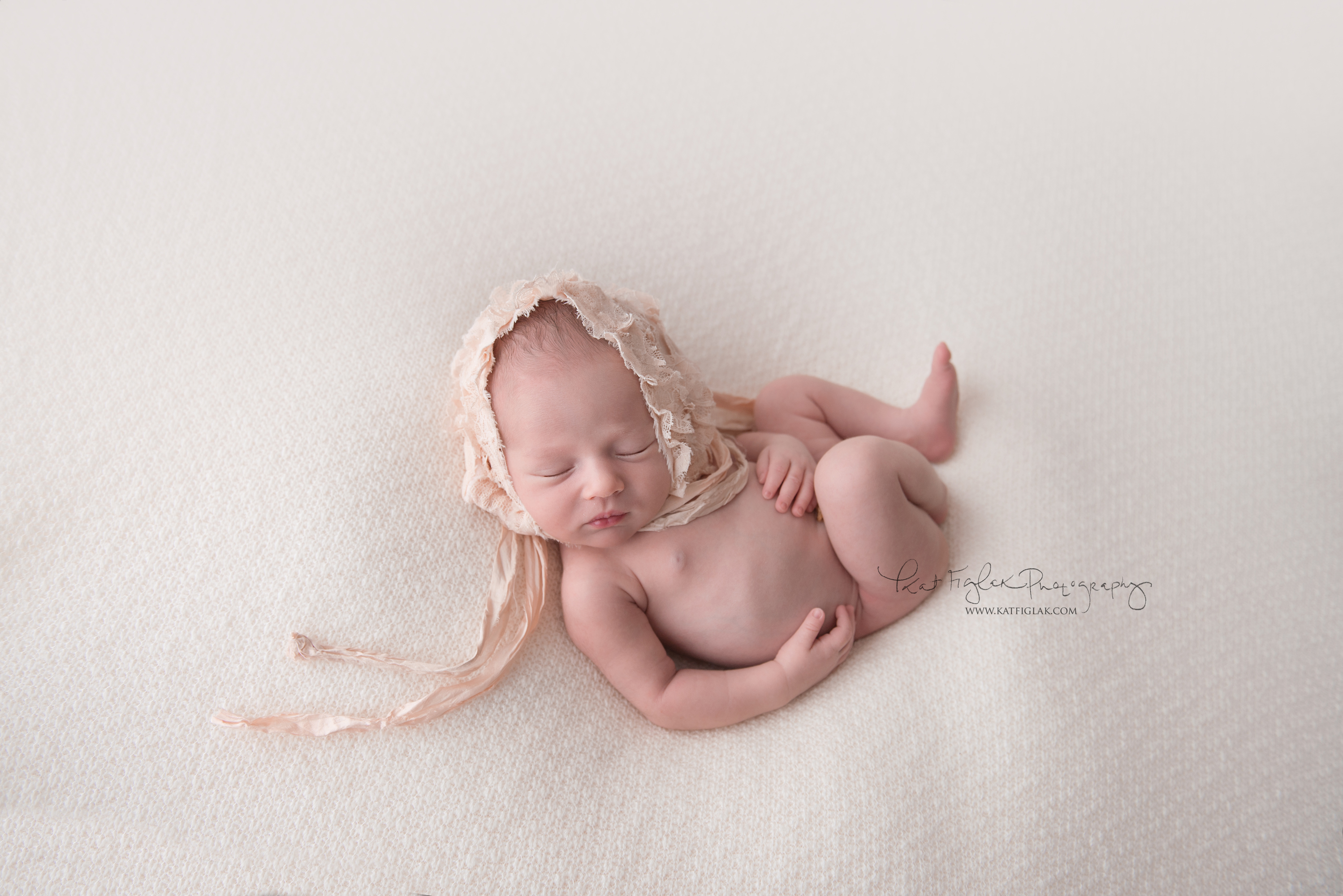 newborn baby girl laying on white knit fabric wearing a blush vintage bonnet