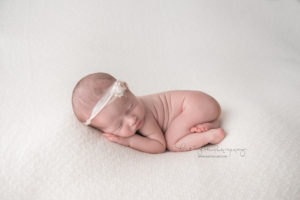 newborn baby girl laying on white knit fabric with white headband