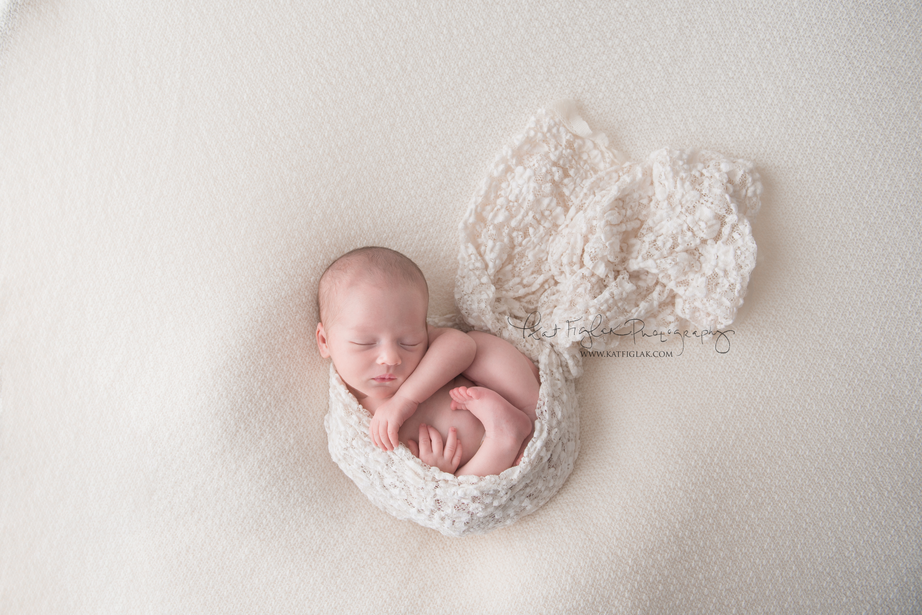 newborn baby girl wrapped in white lace and sleeping on white knit wrap