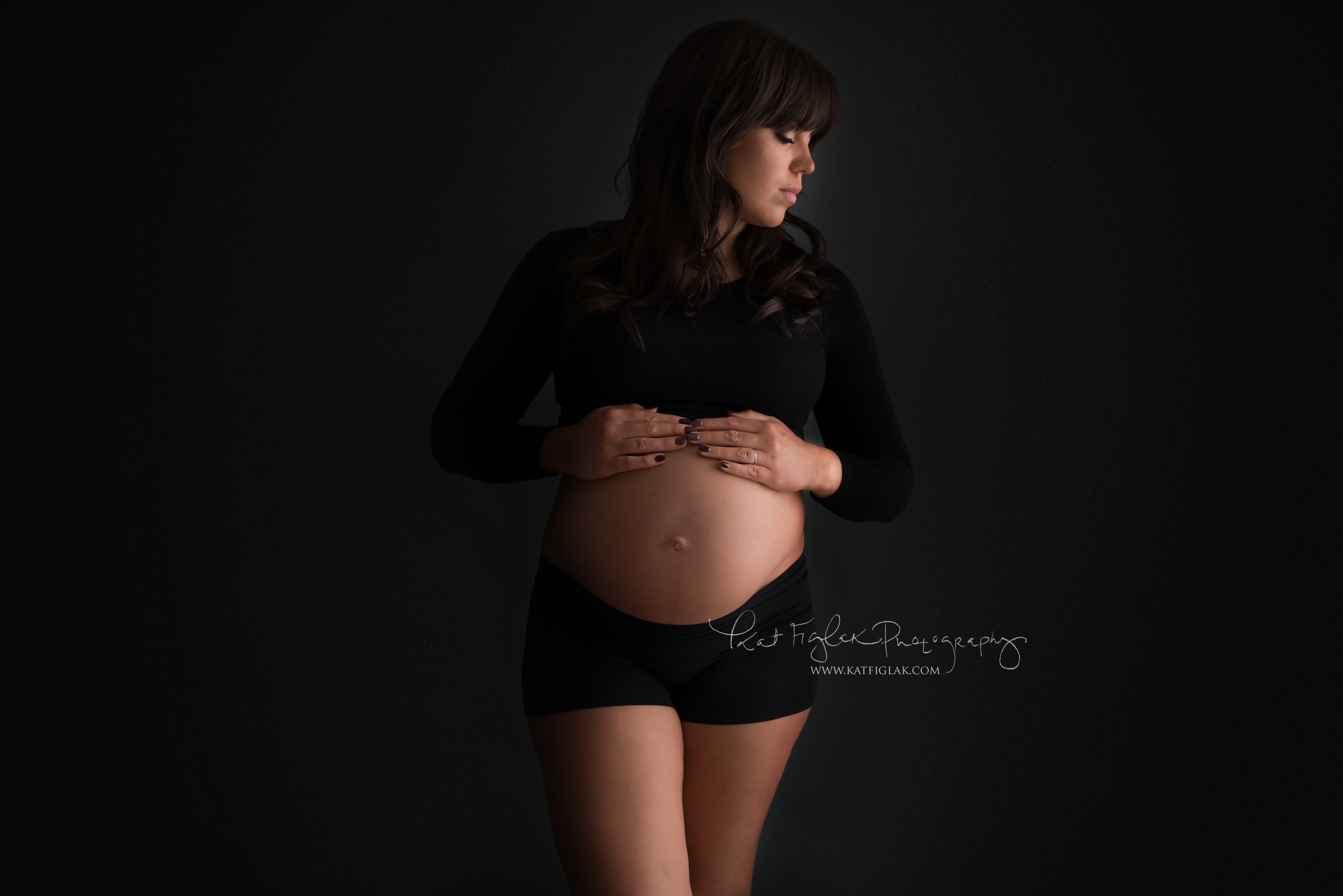 Pregnant woman wearing a black crop top and boyshorts holding her belly