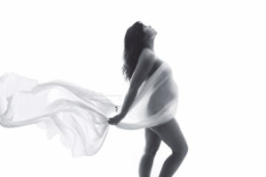 Pregnant mom draped in white silk fabric silhouette shot