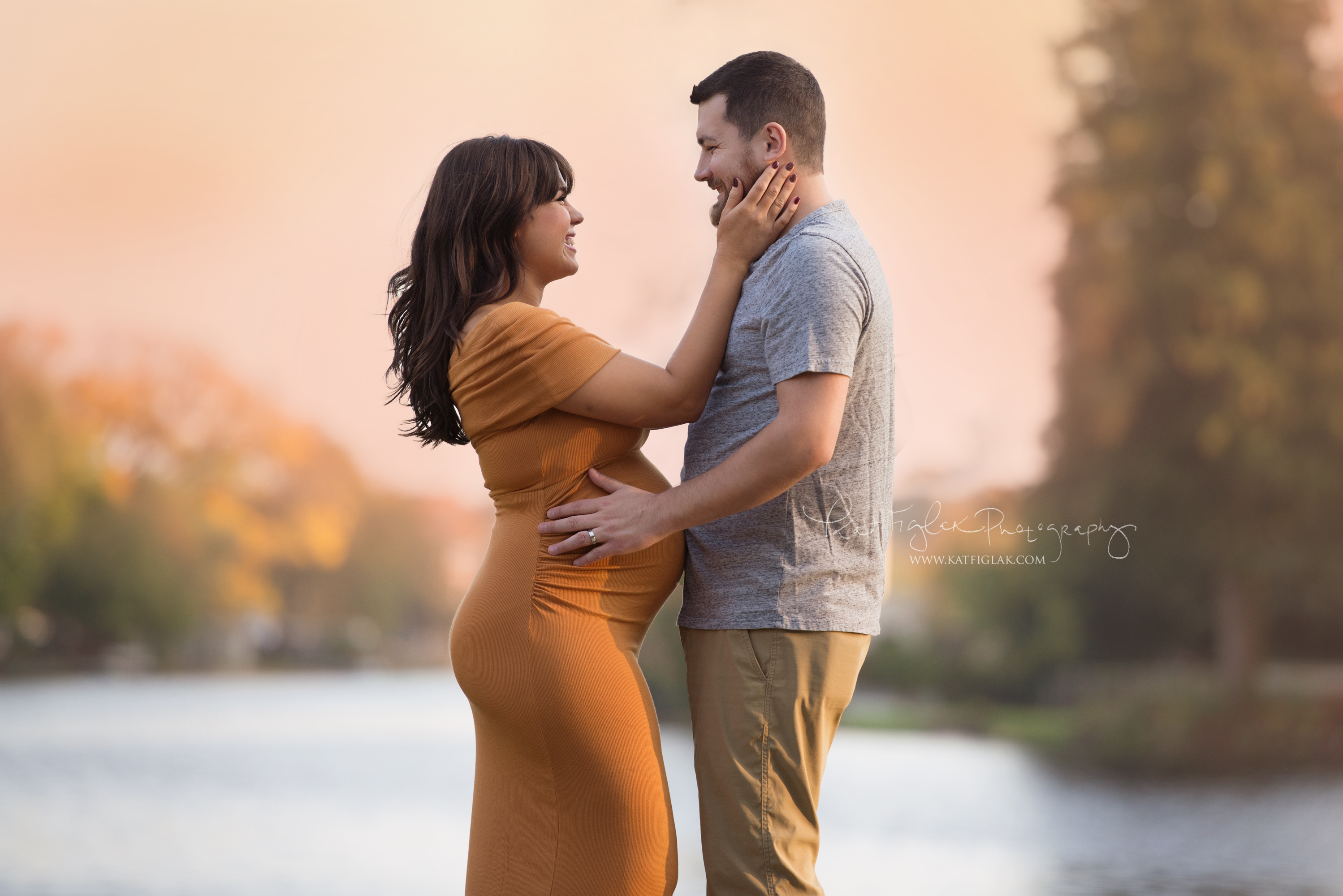 Expecting couple mom wearing a mustard color dress dad with his hands on her belly with sunset in the background