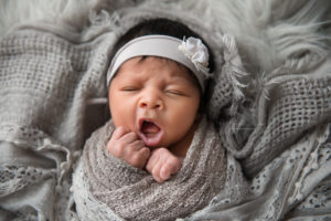 Newborn baby girl laying on gray blanket wrapped in gray lace yawning