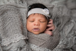 Newborn baby girl sleeping on gray blanket wearing a gray head band