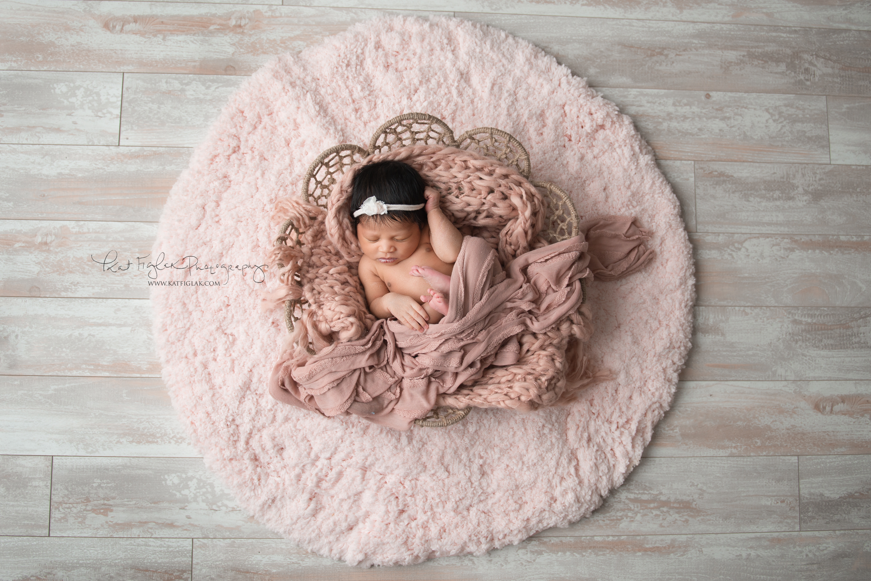baby girl sleeping in blush wraps in a basket on a pink round rug