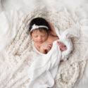 newborn baby girl sleeping in soft white fabrics wrapped in a white wrap with a white headband on