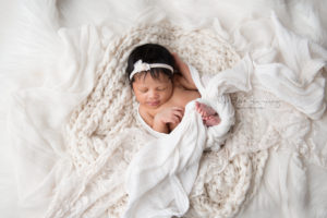 newborn baby girl sleeping in soft white fabrics wrapped in a white wrap with a white headband on
