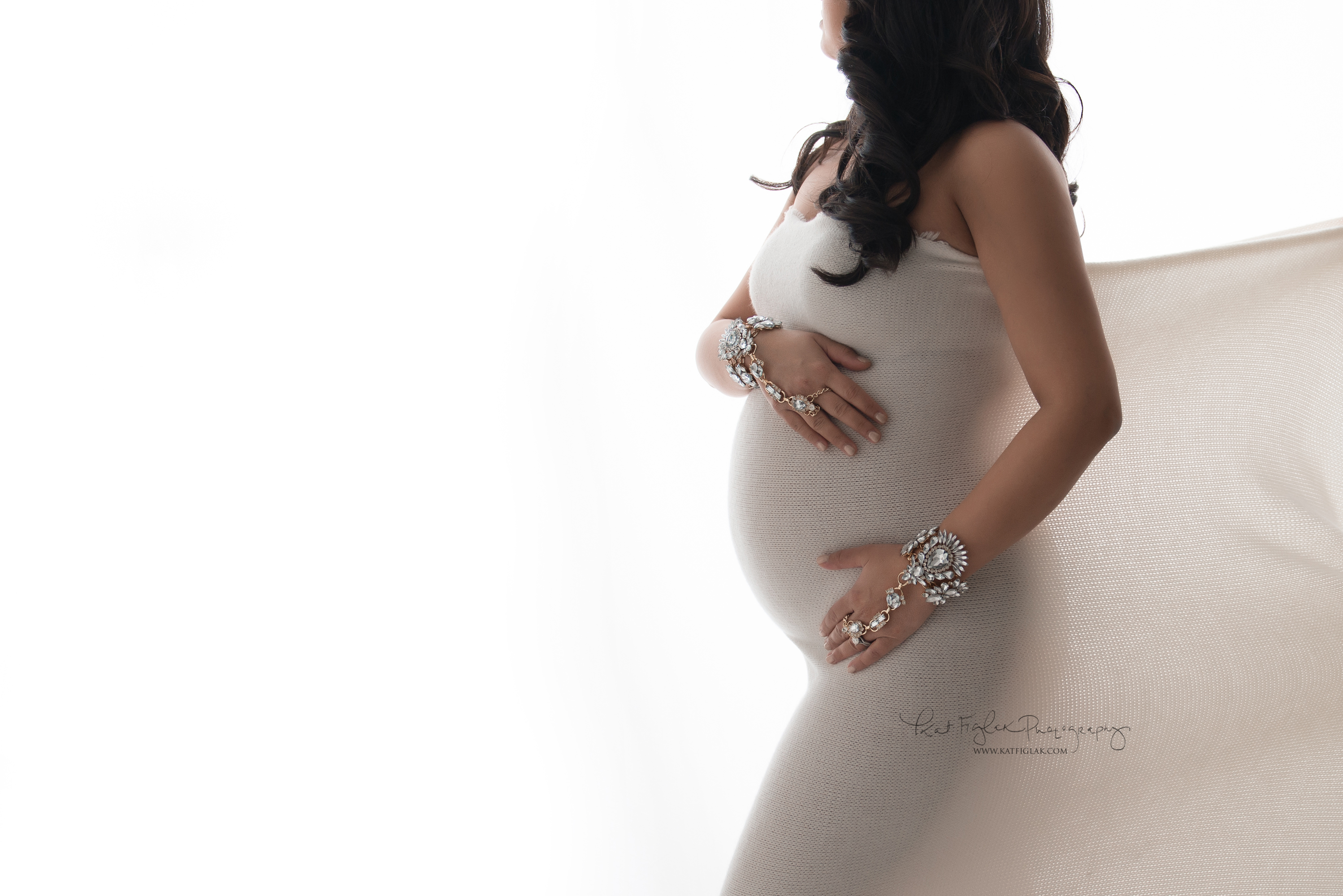 Pregnant mom wrapped in white fabric with hand jewelry 