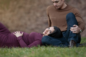 Pregnant mom laying with her husband wearing a purple dress holding her belly