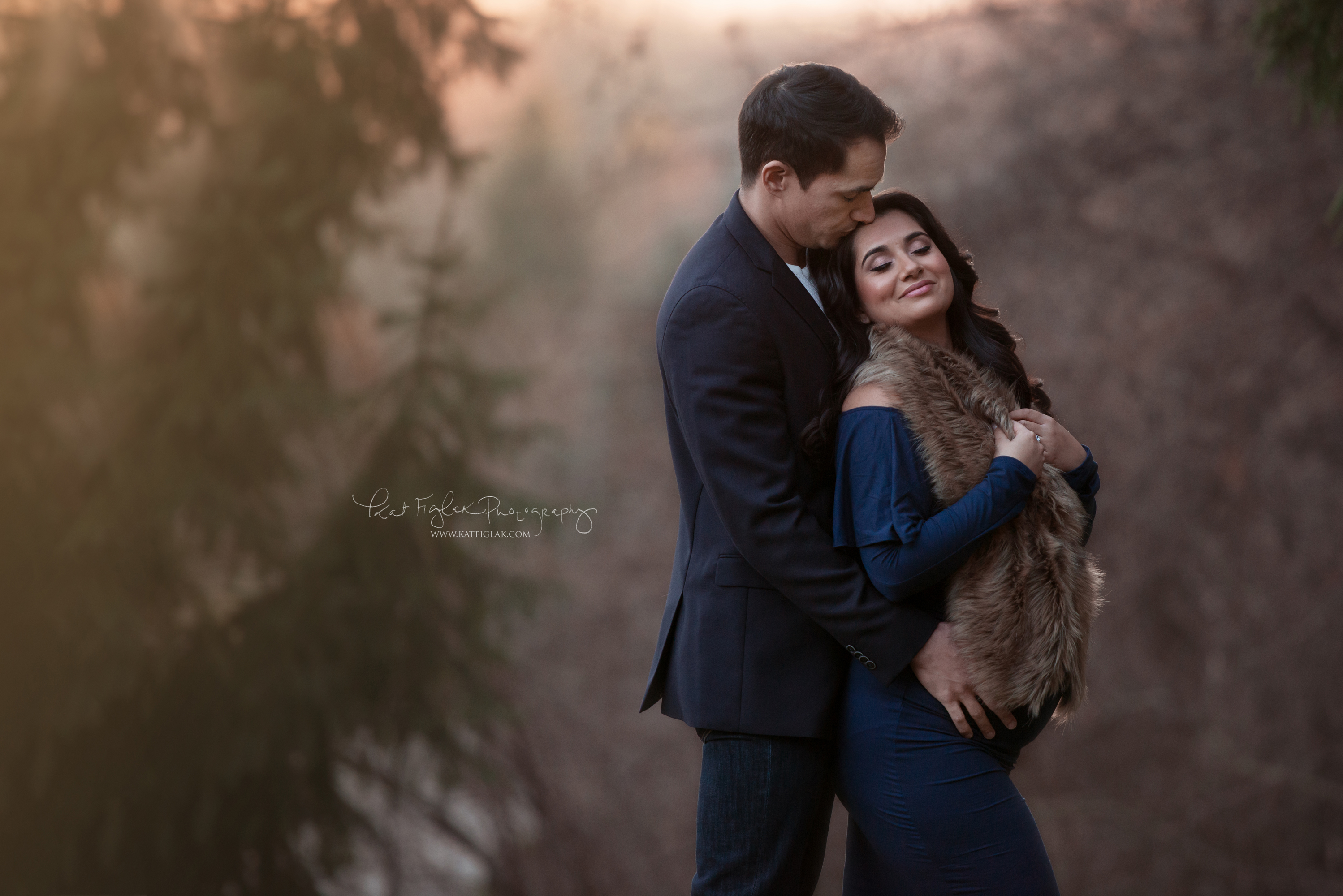 pregnant mom standing with her husband wearing a navy dress draped with fur
