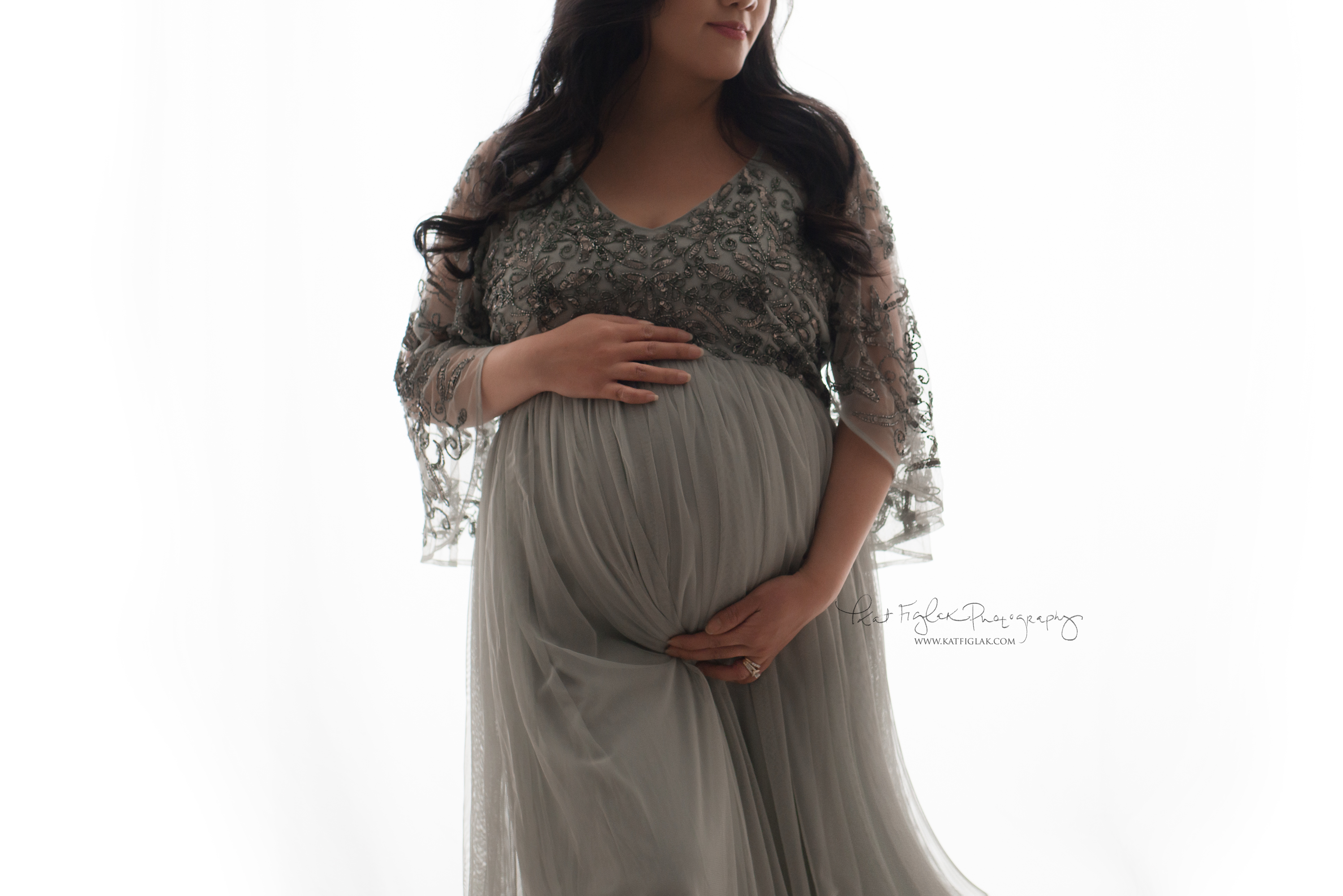 Pregnant mom wearing a sage green beaded gown holding her belly